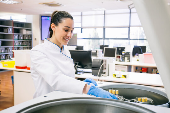 Beautiful young woman in lab robe and putting blood samples in analyzer while working in modern laboratory.