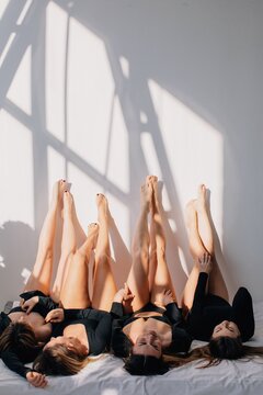 Happy women in black bodysuits lying on bed