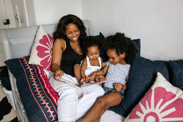 A mother reading with her son & daughter in bed at home.