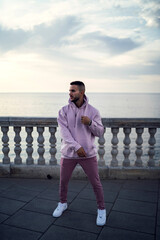 Chico apuesto con ropa actual de color rosa posando en paseo marítimo de cadiz