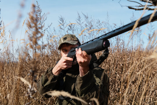 Male hunter aiming rifle in tall grass