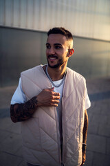Chico joven con tatuajes y ropa aesthetic posando con el atardecer de fondo en cadiz