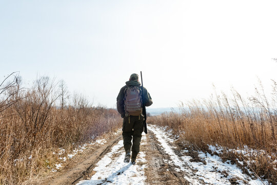Anonymous hunter walking on snowy road on sunny day