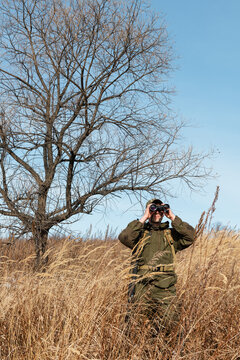 Hunter using binoculars near leafless tree