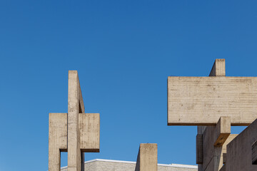 Fototapeta premium Weird, strange and unique abstract shape and form of concrete Brutalist architecture on the rooftop. Massive solid sculptural building of brutalism style against blue sky.