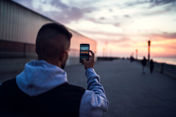 Chico tomando fotos con el smartphone en paseo marítimo cadiz