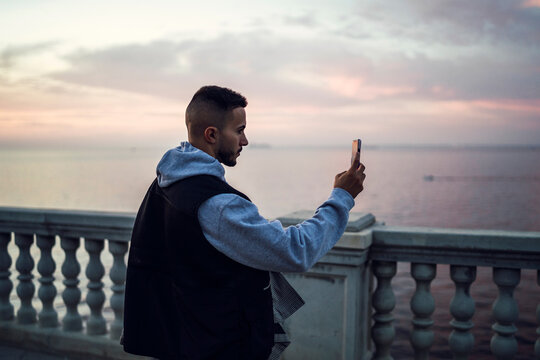 Chico tomando fotos con el smartphone en paseo marítimo cadiz