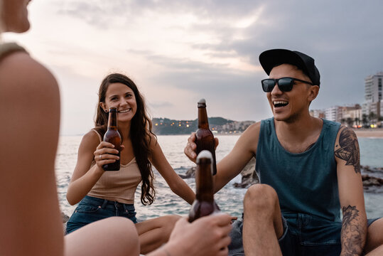 Cheerful couple drinking beer with friend on beach