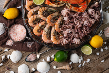 Top view of seafood. Round plate with cooked king crab, shrimps and baby octopuses served with lime, sea salt, seashells on rustic wooden background. Close-up. Thai recipe. Traditional island cuisine.