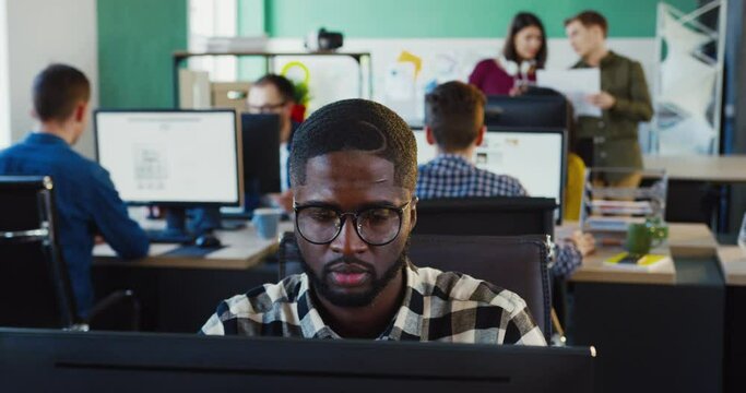 Portrait of young African American working on project and rejoicing in success while sitting in office. Office worker.