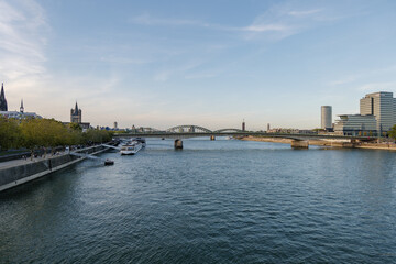 View of Rhine River and riverside, promenade on Rheinboulevard, and background of Hohenzollern Bridge against sunset sky in Köln, Germany.