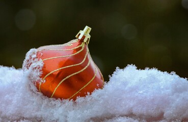 A Christmas decoration red and gold ball ornament  on snow on a green background