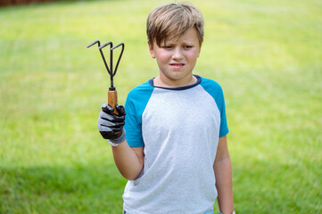 A sad boy with a gardening fork not looking into the camera over the green grass background