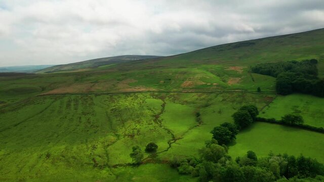 Aerial shot lowering towards the lush green hills located in the english Lake District, bright sunny day.