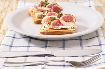 Open sandwich with blue cheese, prosciutto and fresh figs on a white ceramic plate.