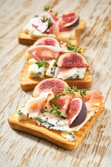 three toasts  with blue cheese, prosciutto and fresh figs  on a white wooden table, vertical composition.