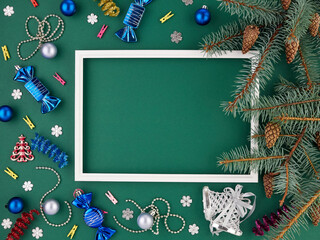 Christmas horizontal background-pine branches lie around a white frame on a green background, with baubles and sweets.Space for text.Congratulations to the new year.