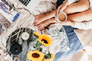 Fototapeta na wymiar Woman is enjoying coffee in the bed. Drinking morning latte and reading. Sunflower arrangement. Bedroom vibe. Autumn season. Feeling home comfortable. Enjoying little things. Fall colors and mood.