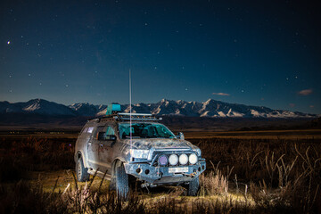 car in field with mountains on background under starry sky at night  © photollurg