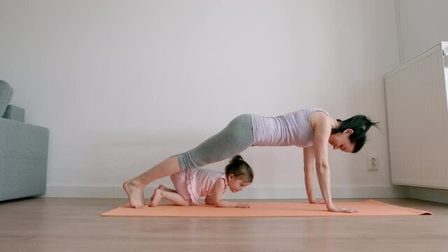 Mother does yoga exercise and little girl plays near at home