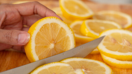 Hand holding a knife cutting Lemon,  The chopping block is full of sliced ​​lemon.
