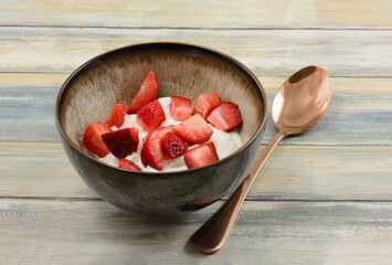 Fresh cut raw strawberries and plain greek yogurt in bowl with copper spoon