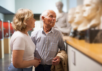 Positive couple of pensioners standing at hall of museum and looking at exhibits