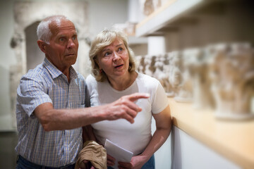 Fototapeta na wymiar Positive elderly couple looking at exhibits on exposition of museum