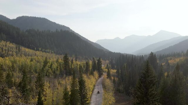 Drone rising up over Utah forest and ATV, mountains in background