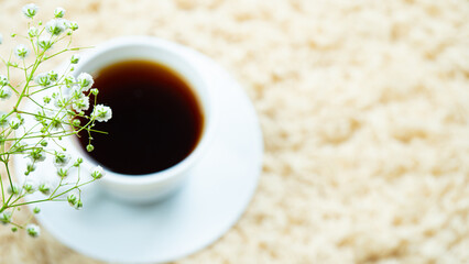 White cup with black coffee placed on a cream carpet. Decorated with white flowers in the corner of the coffee. 