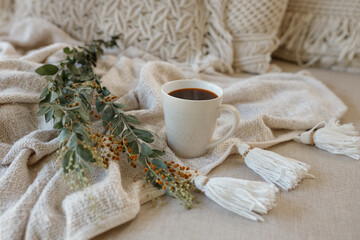 Autumn or winter composition. Cup of coffee, dried autumn leaves, knitted blanket on white sofa