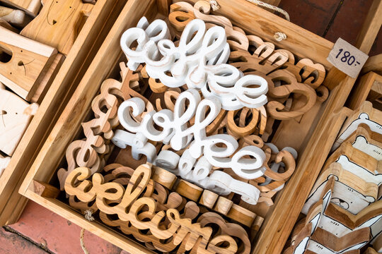 Stack of wooden alphabet sign in cursive writing which reads "coffee", "hello", and "welcome" in natural and white color displayed in a wooden tray.
