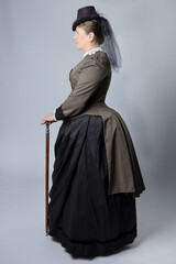 A middle-aged woman dressed in a Victorian costume and holding a fob watch and a walking cane