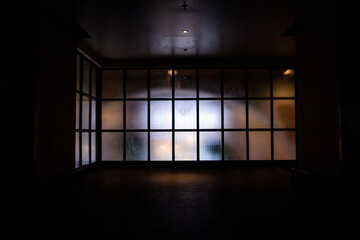 Frosted glass wall with black metal frame in grid pattern with bright light from the inside looking from the hallway.
