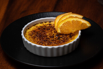 Creme caramel, burnt cream with orange on the dark wood table. French vanilla cream dessert with caramelized sugar on top on the white plate.