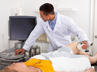 Young smiling man sonographer using ultrasonography machine checking female patient in hospital diagnostic room