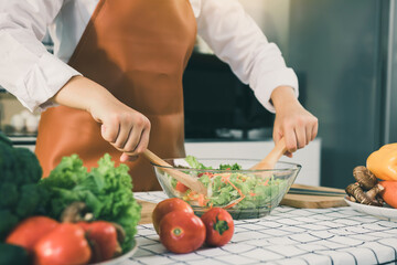 Asian woman is mixing the ingredients in a salad bowl at the kitchen cooking table.