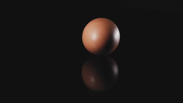Egg is spinning on a black background. Slow motion of an egg in a shell spinning in a circle on a dark table. Close shot of a spinning egg.