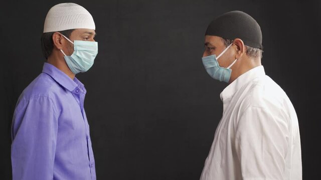Two muslim men in medical mask greeting or salam each other in Islamic way while Maintaining social distancing - Concept of Coronavirus or covid-19 safety measures and new normal lifestyle