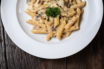 Homemade delicious pasta macaroni with white mushrooms chicken meet mushrooms in creamy cheese sauce in the white plate on the dark brown wood table. Parsley, spicy. Yellow, green.