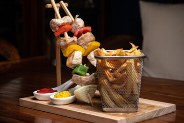 Meat beef kebab with vegetables and spices with barbecue sauce and ketchup, mustard on a dark background on a wooden cutting board. BBQ meat. Fish kebab with bell pepper. French fry
