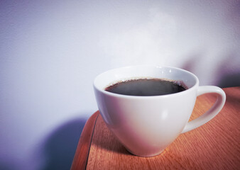 Intense black coffee in a white mug placed at the corner of a wooden desk. Refreshing coffee before working at home.