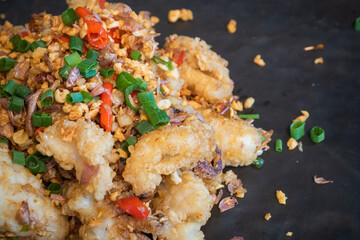 Deep fried sea bass with chili and salt in a black plate, served on the dining table. Snapper is a diet that helps you lose weight and improve your brain.