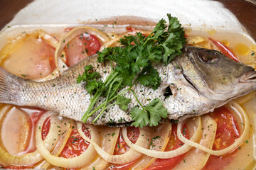 Marinated grilled whole sea baked fish with tomato, onion, parley, lemon, sauteed vegetables. Food on a white plate. 