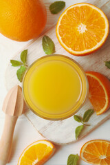 Board with glass of orange juice, oranges and juicer on wooden background