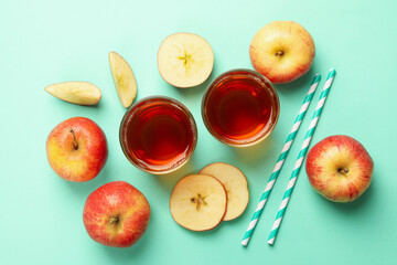 Apple slices, straws and glasses of apple juice on mint background