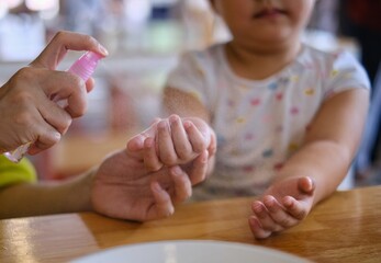 A mother spraying alcohol cleansing spray on her young daughter's hands before eating a meal.