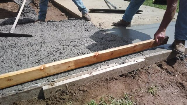 men screed cement using a 2 x 4