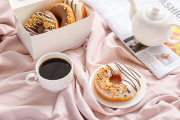 Composition with tasty donuts and coffee on bed