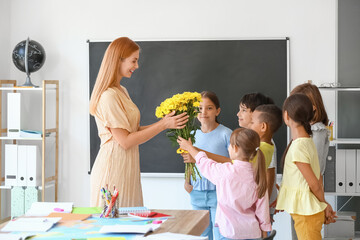Schoolchildren greeting their teacher in classroom - obrazy, fototapety, plakaty